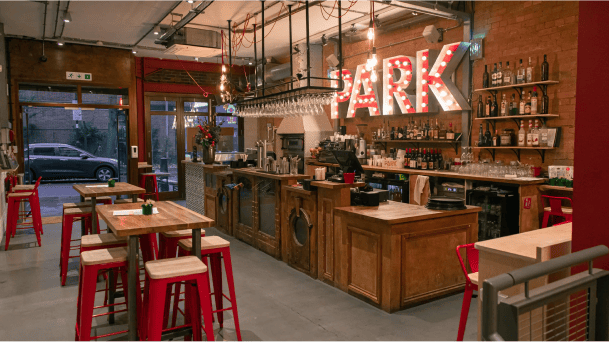 Park Theatre downstairs L shaped bar with large Park Pizza Logo lit up with while bulb lights in the letters of the logo