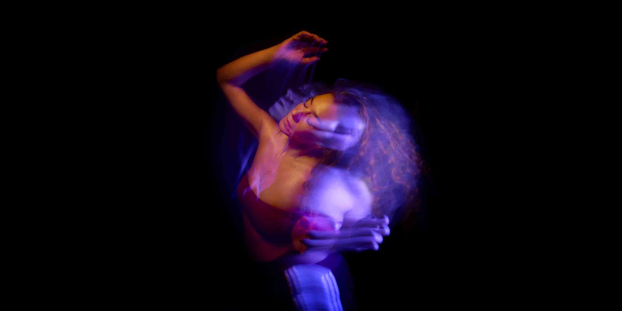 A woman dances in purple light against a black background.
