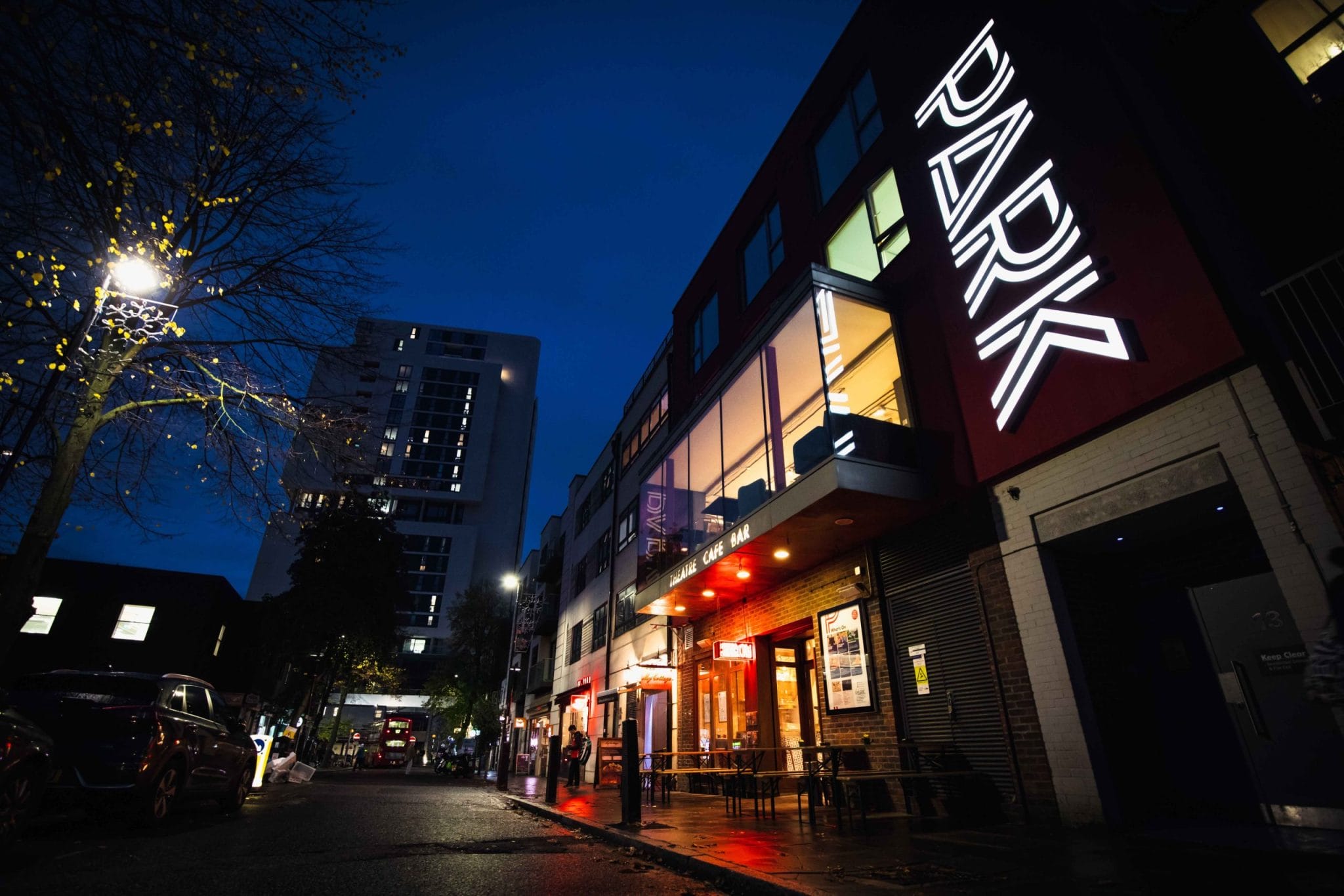 Park Theatre Building, Park logo on the side of the building and a large window on the second floor of the building, underneath the window it says Theatre, Cafe and Bar with outside seating at the front of the building on the ground floor