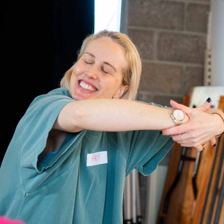 A woman in a blue T-shirt is holding her arms in a circle, giving an imaginary hug.