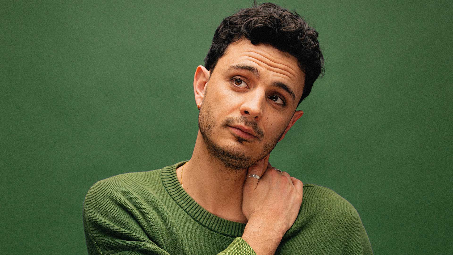 Pedro Leandro in a green top has his head cocked to one side thoughtfully. He rests one hand on his shoulder.