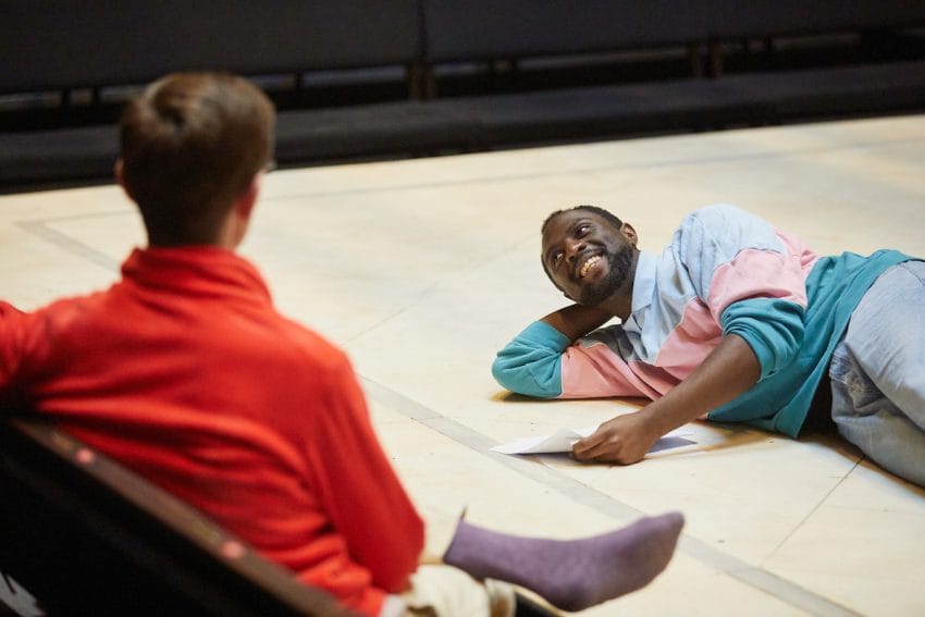 A man lies on the stage floor holding the script smiling