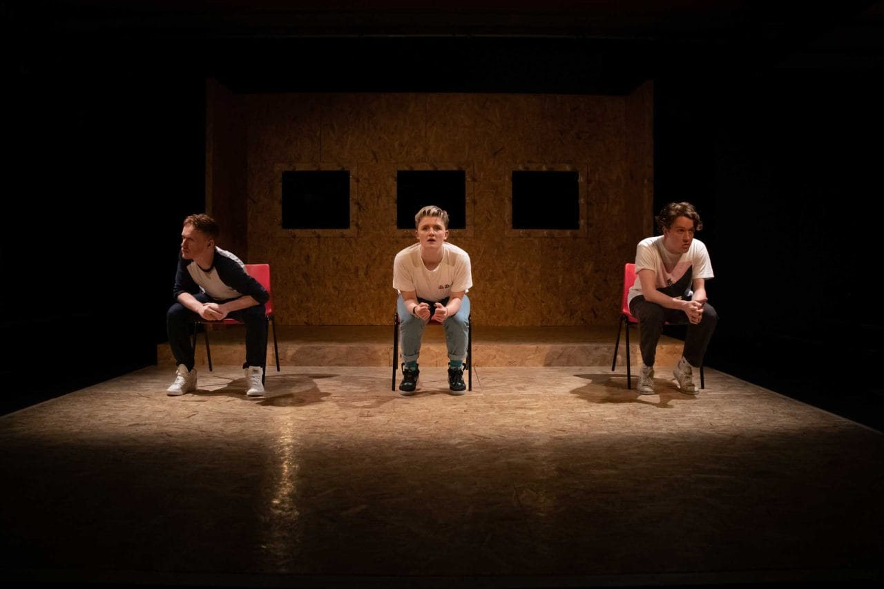 A production image of 3 people sitting on chairs facing the audience leaning forward intensely speaking to the audience