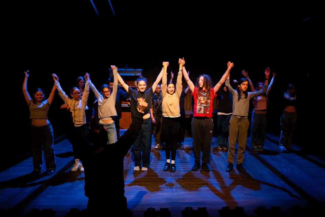 Photo of young actors and actresses standing on stage preparing to take their bows