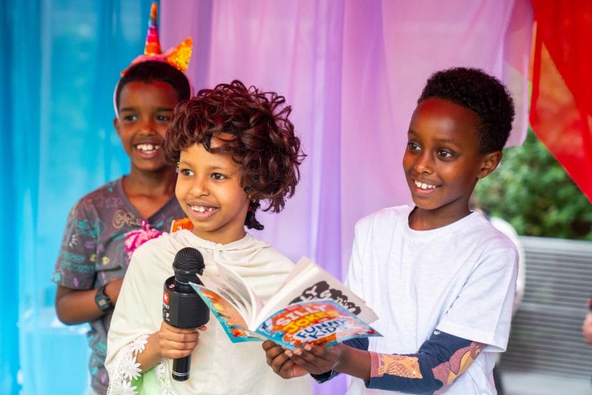 A photo of three kids with one holding a microphone and one holding a joke book.
