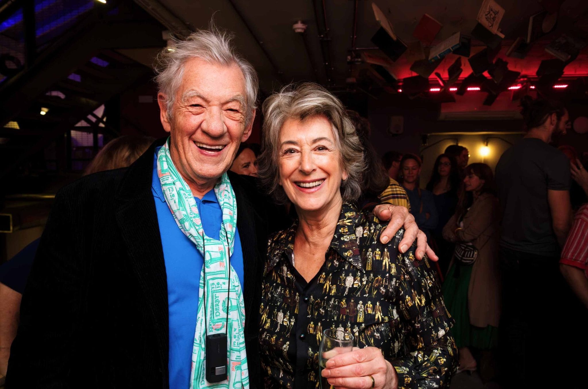 Sir Ian Mckellen smiling with his arm on the shoulder of a woman
