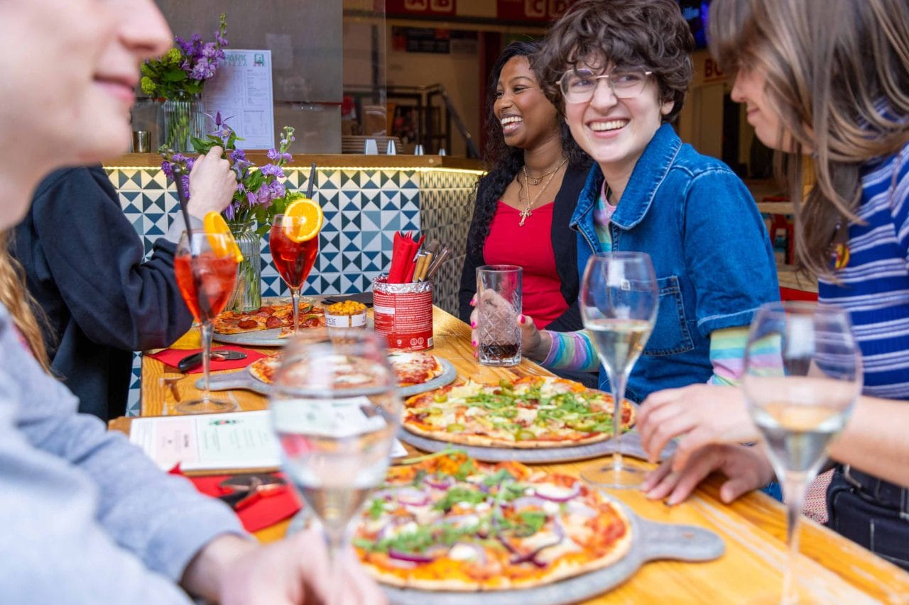 Photo of people enjoying pizza and drinks laughing and chatting