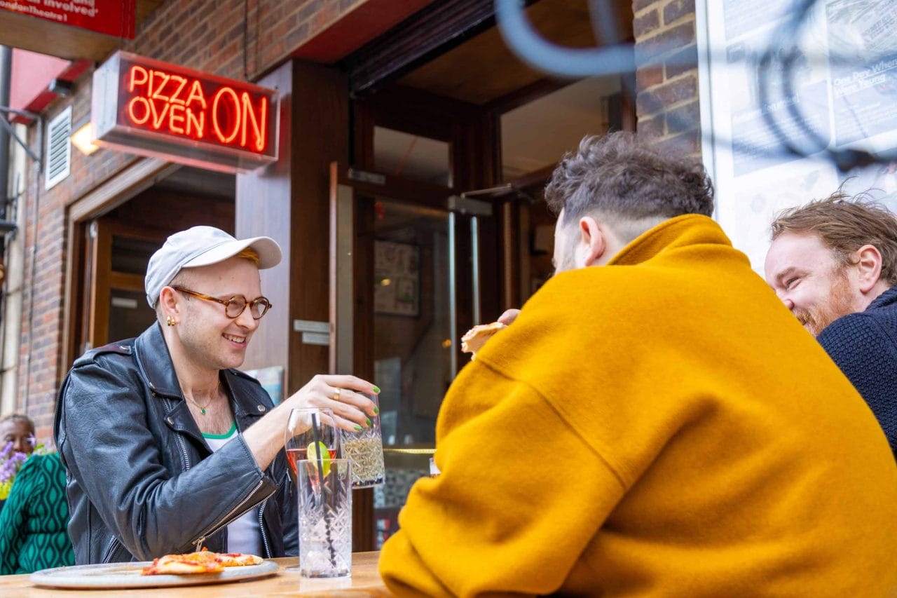 Photo of people enjoying pizza and drinks sitting in the outside seating area of Park Theatre