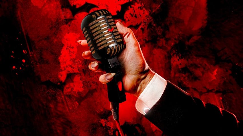A hand with long nails vampire nails holds a microphone with a red bat on it. The background shows red clouds.