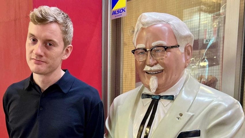 A photo of comedian James Acaster standing next to Colonel Sanders