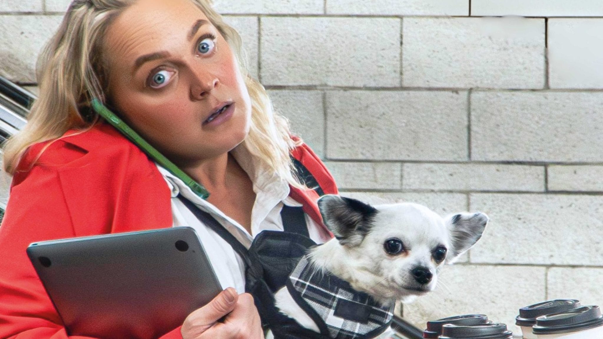 A woman holds a dog and struggles with holding a phone to her ear.