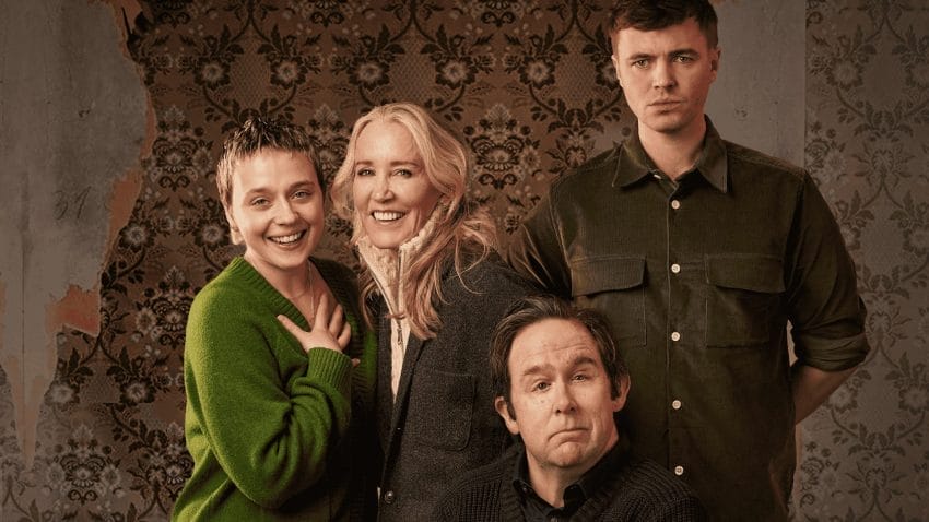 Four people face forward. Two women, smiling, appearing happy, with a taller young man, standing to their left, looking mildly confused or concerned. A second, older man, sits in the portrait, with a slight grin. The backdrop sees unattractive, partly ripped brown wallpaper.